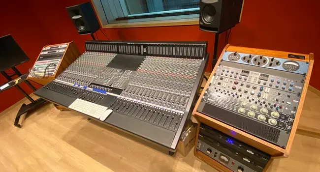 Sala de control del estudio de grabación de la Universidad Anáhuac Querétaro, con una consola de mezcla analógica, dos monitores de estudio y un rack de equipo de audio.