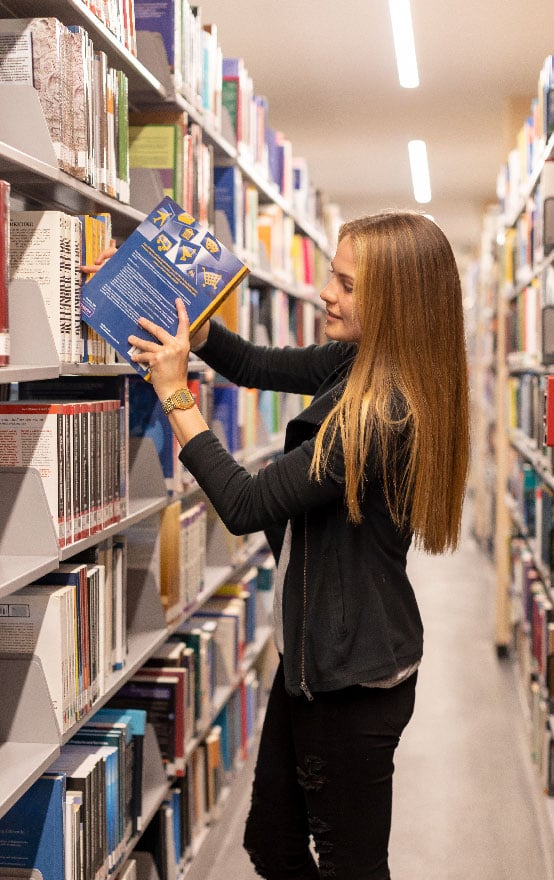 Alumna explorando libros en la biblioteca de la Universidad Anáhuac Querétaro en busca de conocimiento y recursos académicos.