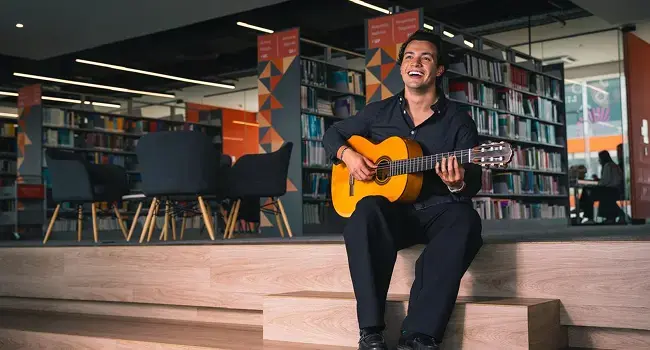 Hombre tocando una guitarra sentado con un fondo de biblioteca