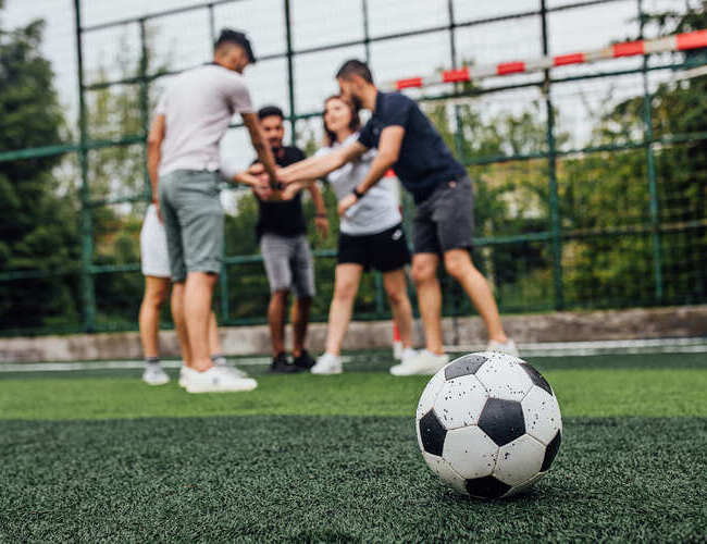 close-up-football-ball-green-field-players-going-playing-together(1)(1)(1)