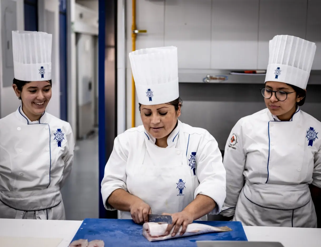 Maestra de gastronomía haciendo una demostración de técnicas culinarias a sus estudiantes