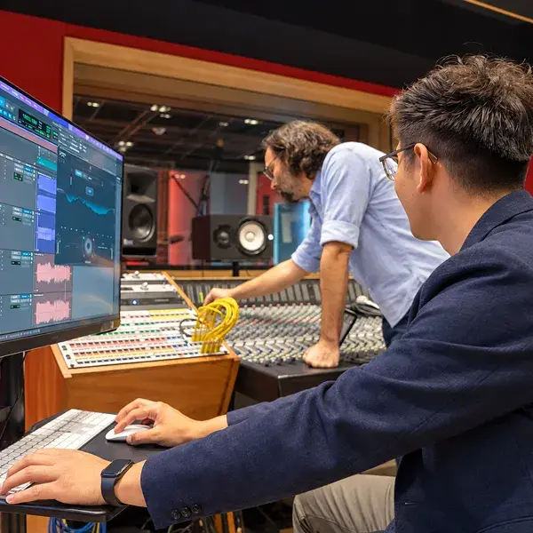 En un estudio de grabación rojo maestro esta tocando el sistema de audio mientras el estudiante toca la computadora donde se graba la música 