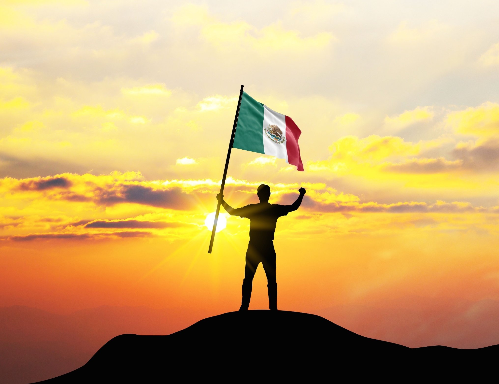 Estudiante en la cima de una montaña ondeando la bandera de México por la Independencia