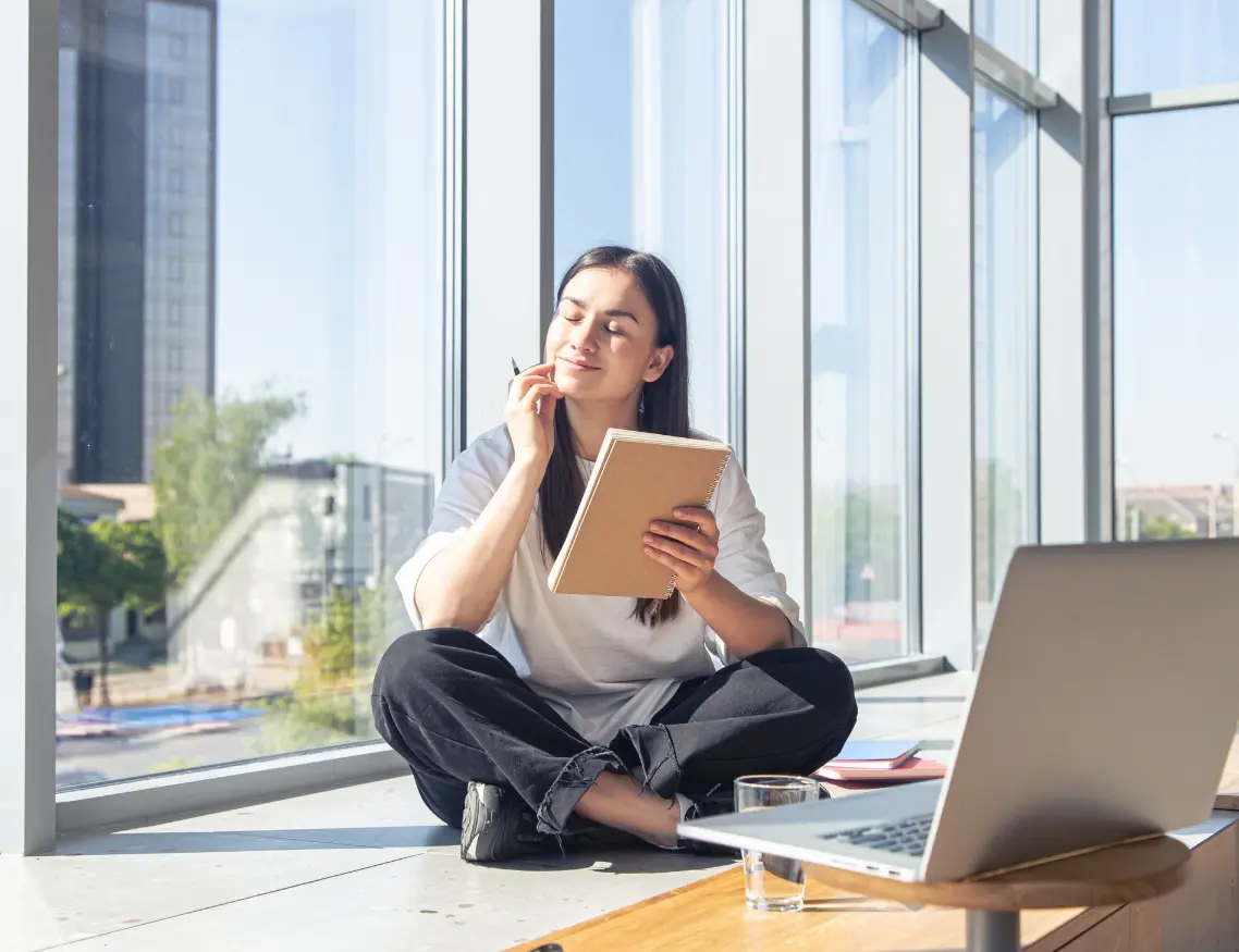 Chica joven sentada frente a un ventanal disfrutando de las ventajas de haber estudiado diseño gráfico